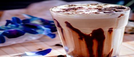 A tall glass of layered beverage with chocolate drizzle on a wooden surface.
