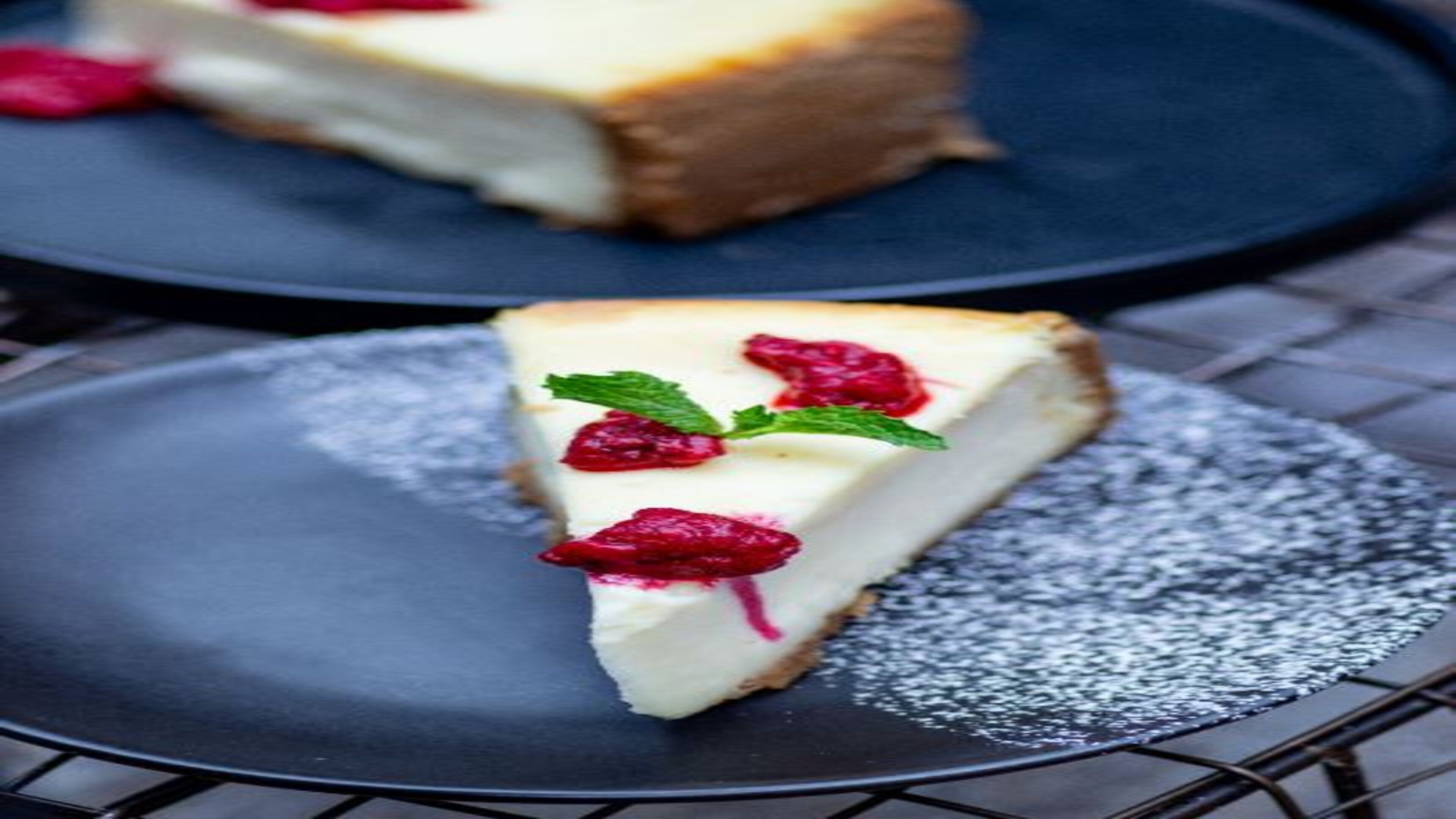 A slice of cheesecake on a plate with powdered sugar and raspberries.