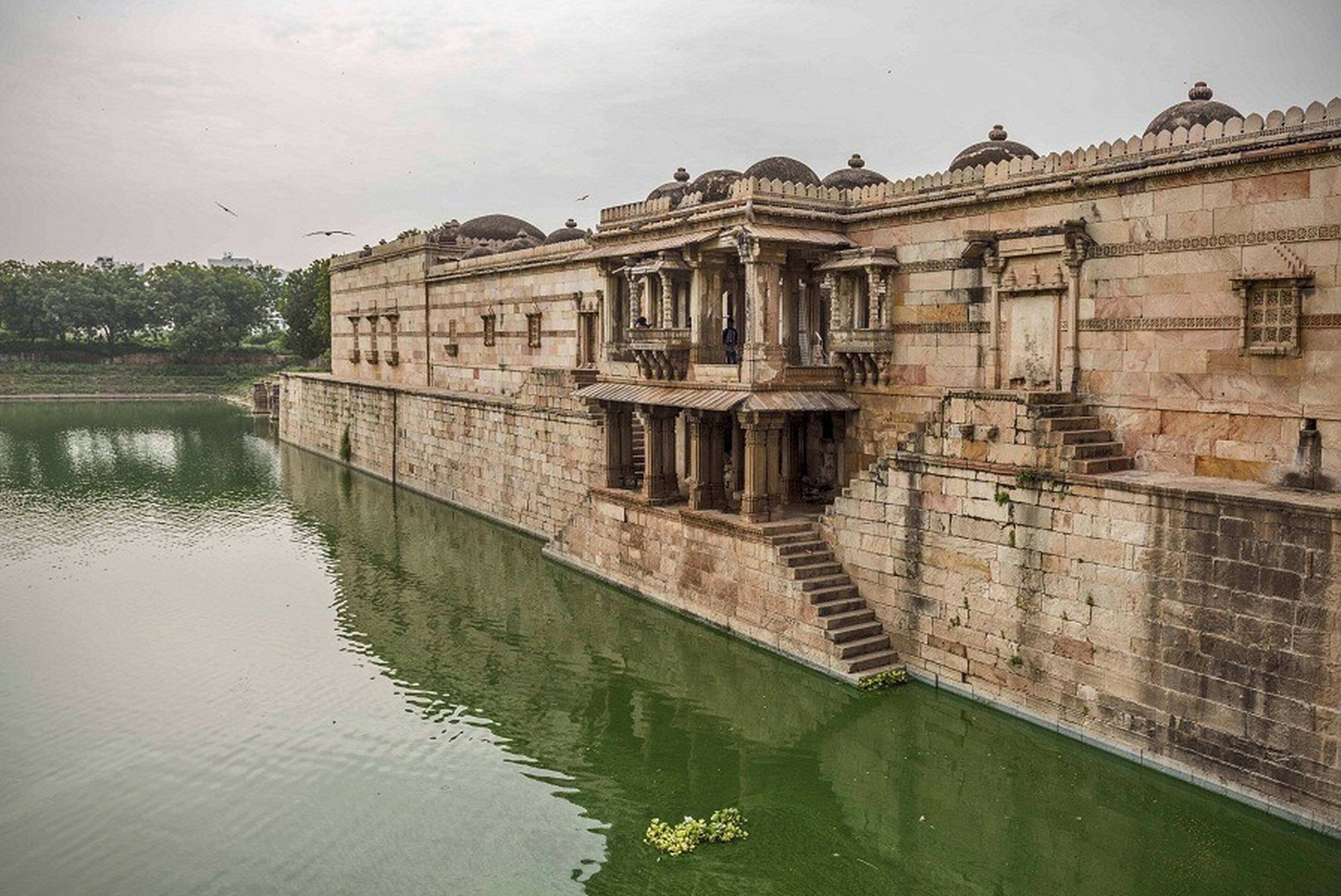 A historic building with a water body in front, featuring ornate architecture and a staircase leading to an upper level.