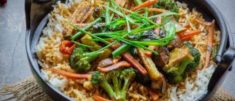 A bowl of fried rice with vegetables and meat, placed on a dark surface with a rustic burlap cloth underneath.