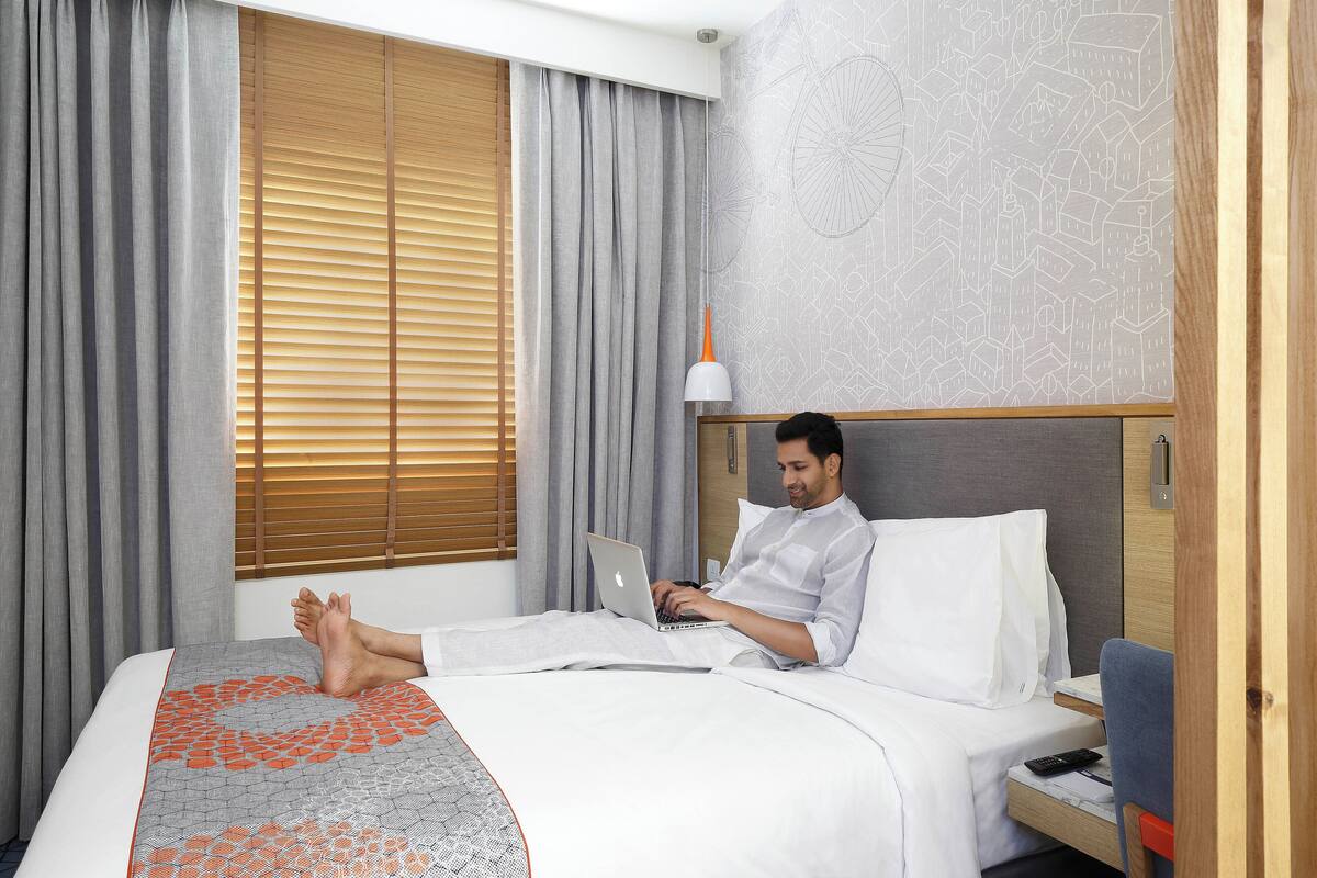 A hotel room with a bed, a laptop, a bedside table, and a nightstand.
