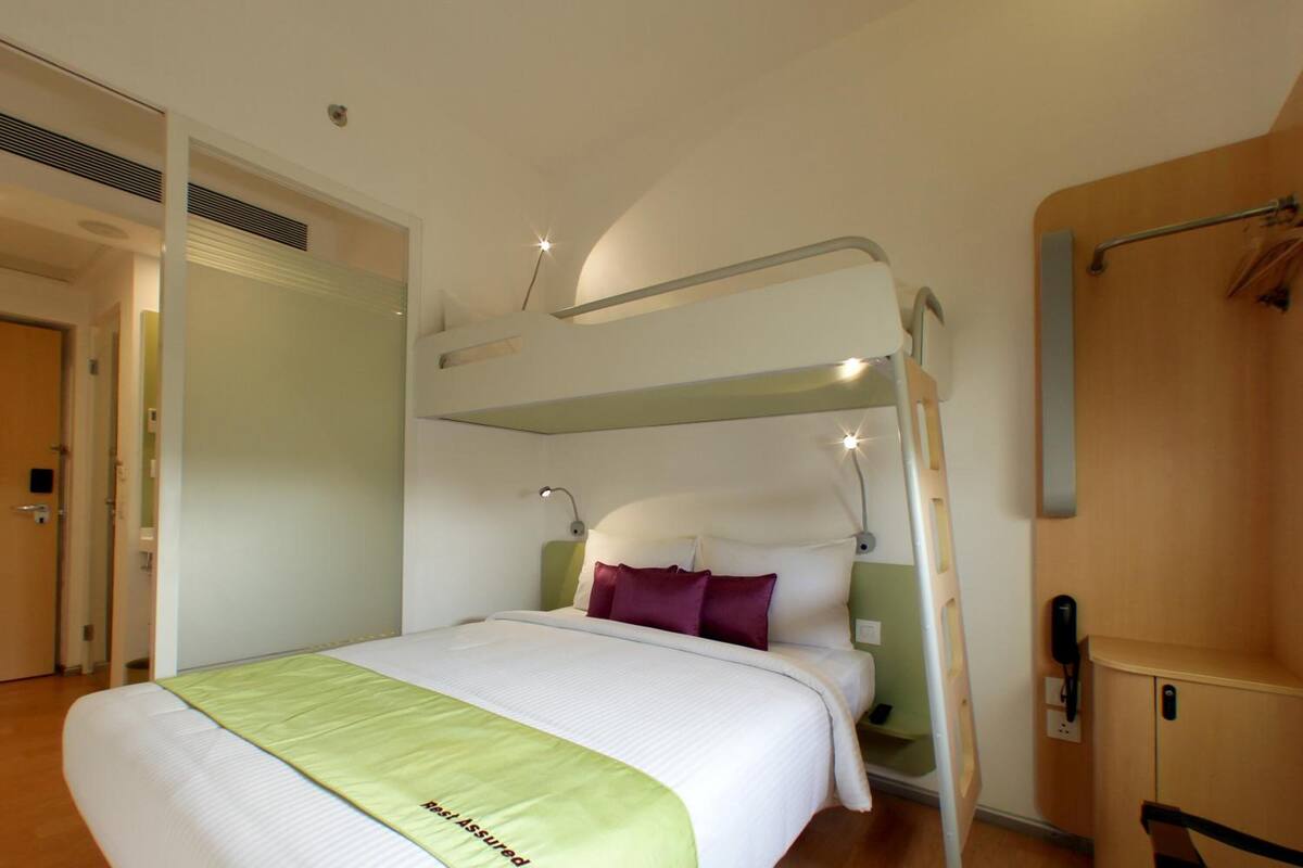 A bunk bed room with a green bedspread, a bedside table, and a wall-mounted phone.