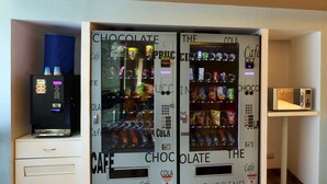 A room with two vending machines labeled 'Chocolate' and 'The Cappuccino' offering various snacks and drinks. - Hotel Caspia Pro Greater Noida (Greater Noida)