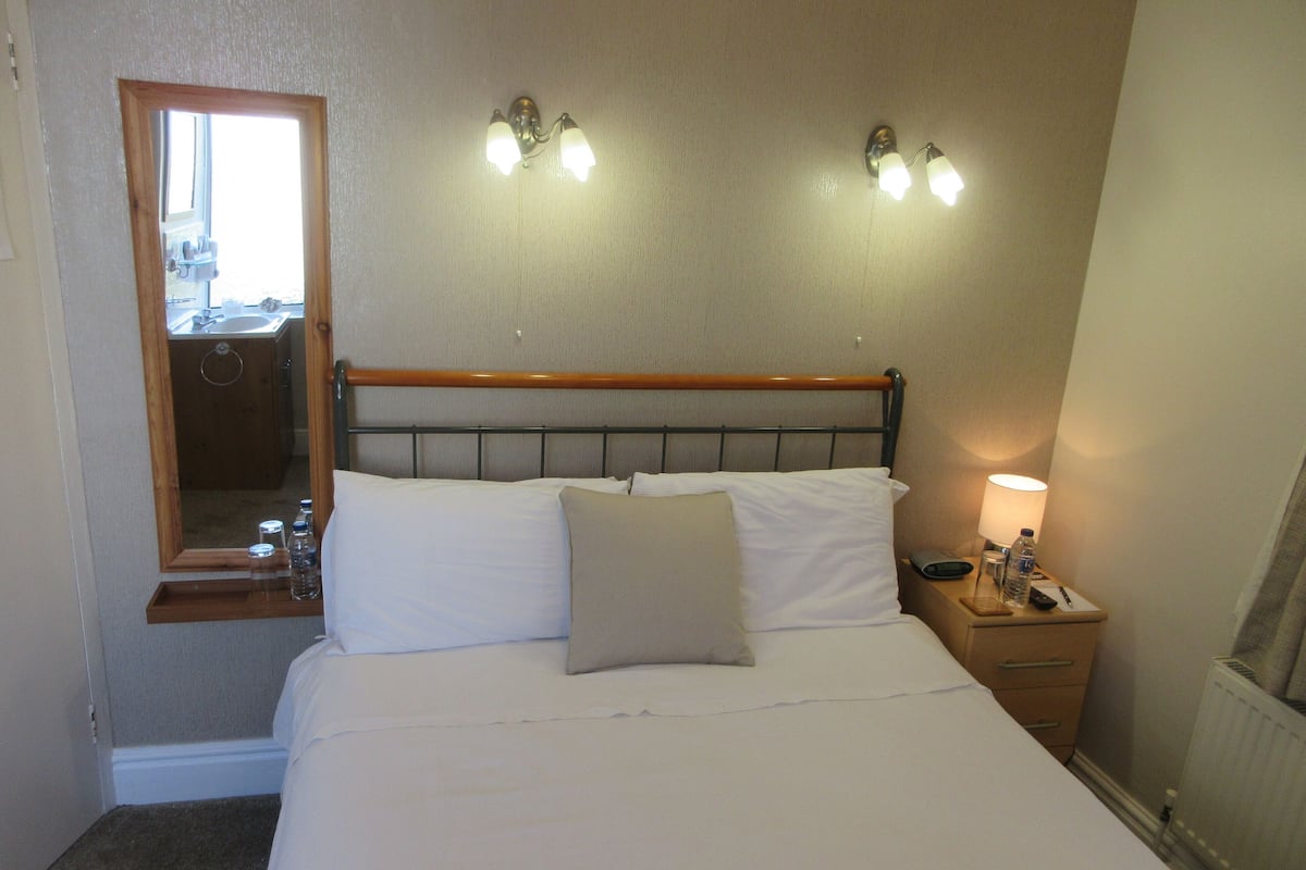 A hotel room with a bed, bedside table, lamp, and a mirror.