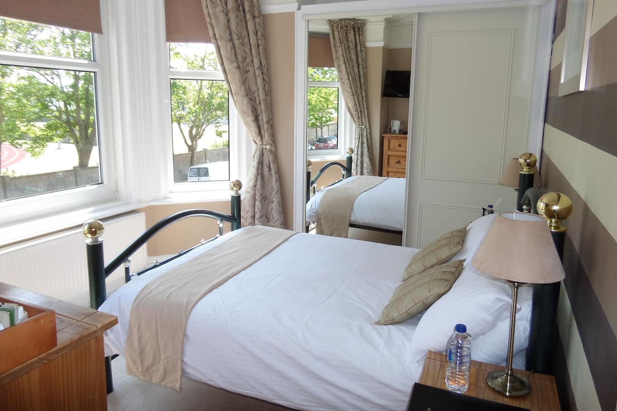A hotel room with a bed, bedside table, lamp, and a view of the outside.