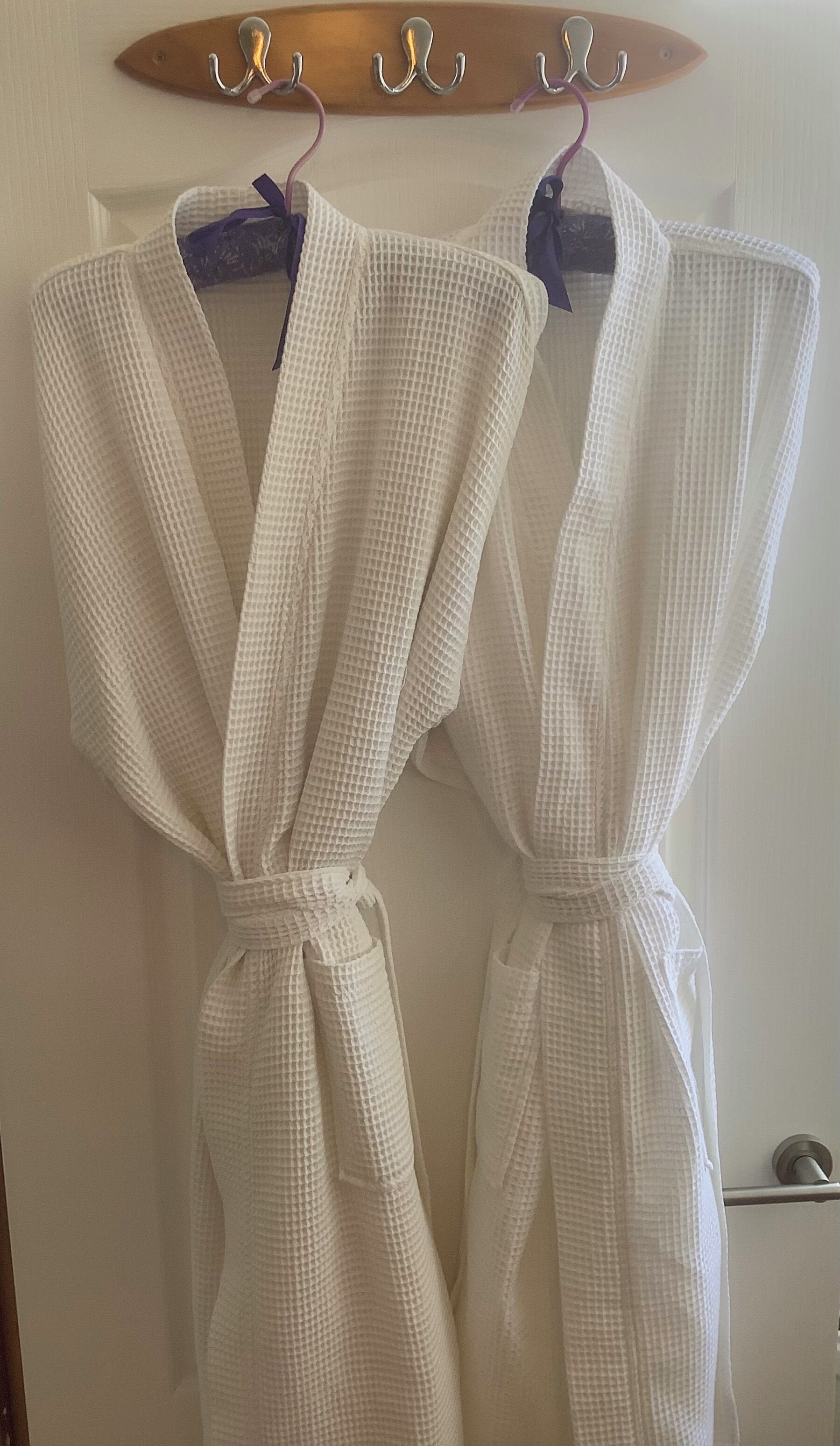 Deux robes blanches sont suspendues à un portant en bois.
