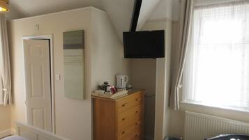 Ein Schlafzimmer mit einem Bett, einer Kommode, einem an der Wand befestigten Fernseher, einem Heizkörper und einem Fenster mit Vorhängen.