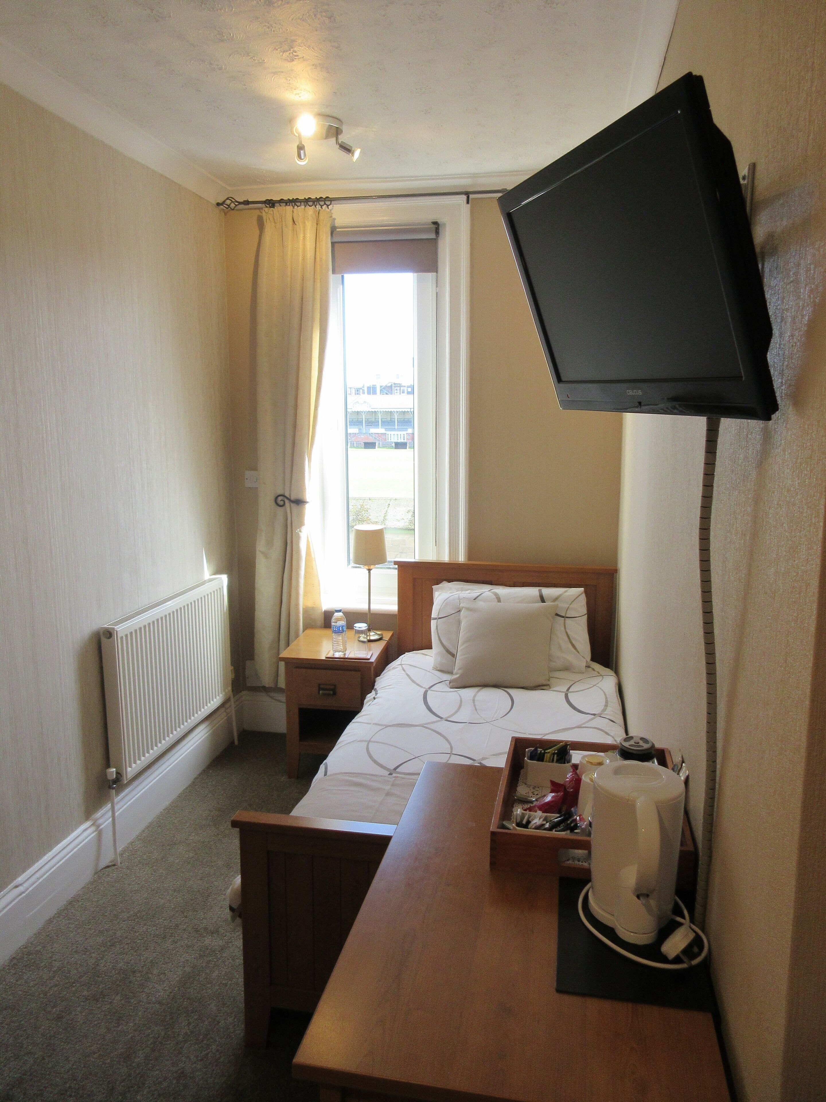 Ein Hotelzimmer mit Bett, Nachttisch, Lampe und einem an der Wand befestigten Flachbildfernseher.