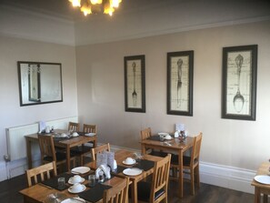 A dining area with wooden tables and chairs, white tableware, and framed wall art. - Beaumont House (Great Yarmouth)