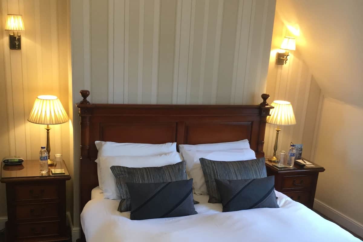 A neatly made bed with a dark red bedspread, two bedside tables with lamps, and a wooden headboard.