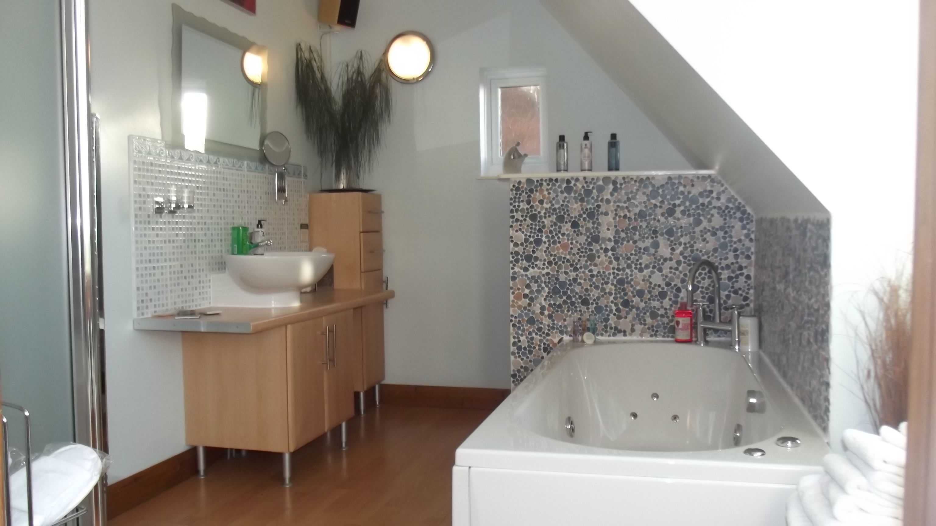 A modern bathroom with a freestanding bathtub, a sink with a mirror, wooden cabinets, and a tiled backsplash.