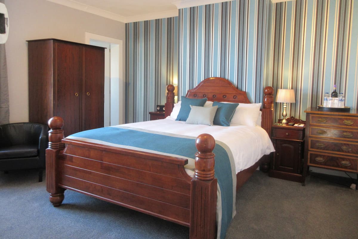 A hotel room with a large wooden bed, a nightstand with a lamp, a dresser, and a striped wallpaper wall.