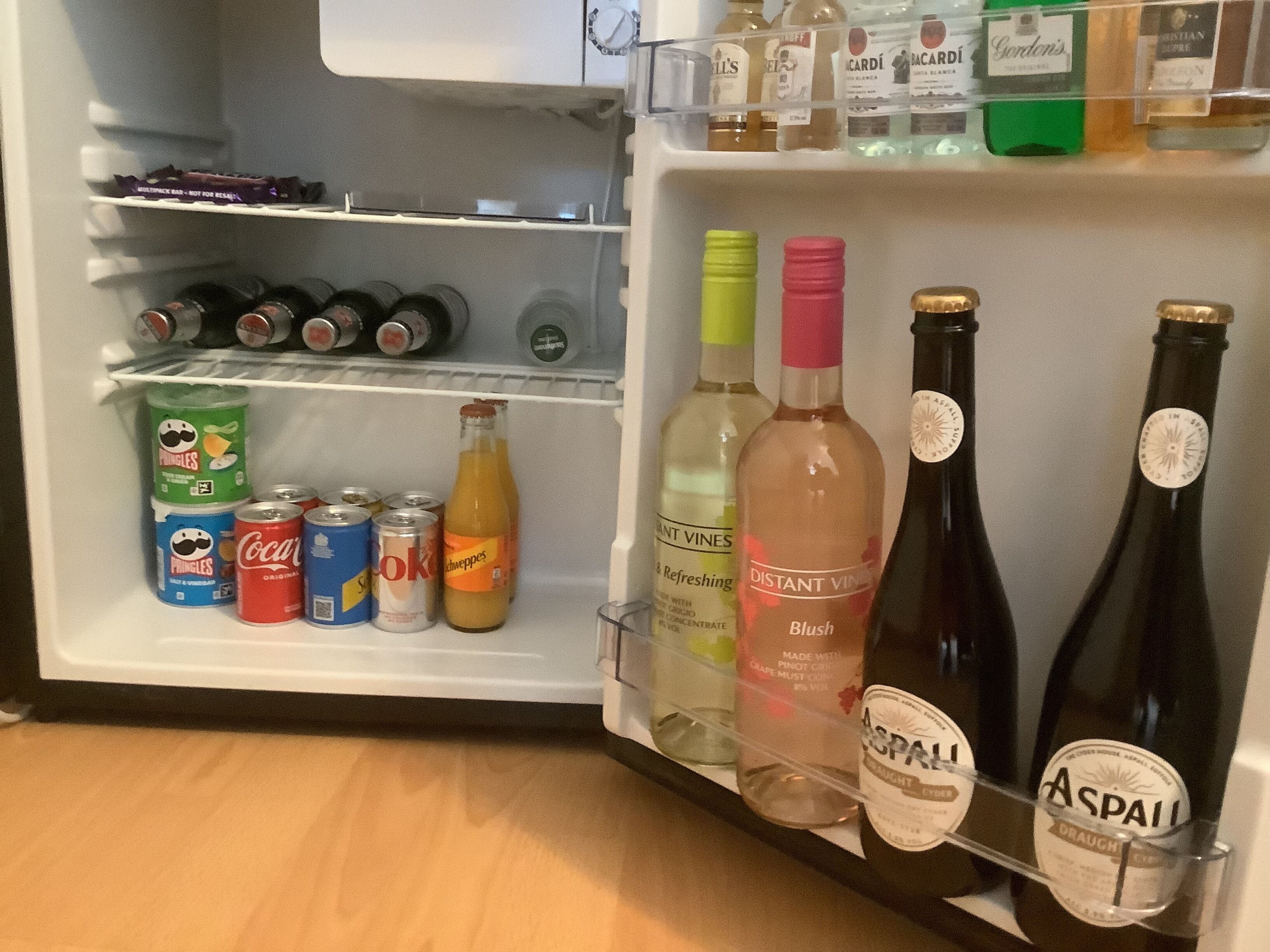 Un réfrigérateur rempli de boissons, notamment des canettes de soda, des bouteilles de vin et une bouteille de schnaps.