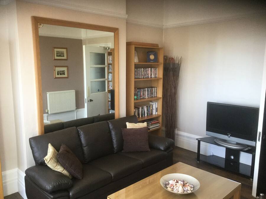 A living room with a black leather sofa, a wooden coffee table, a bookshelf, a television, and a mirror.