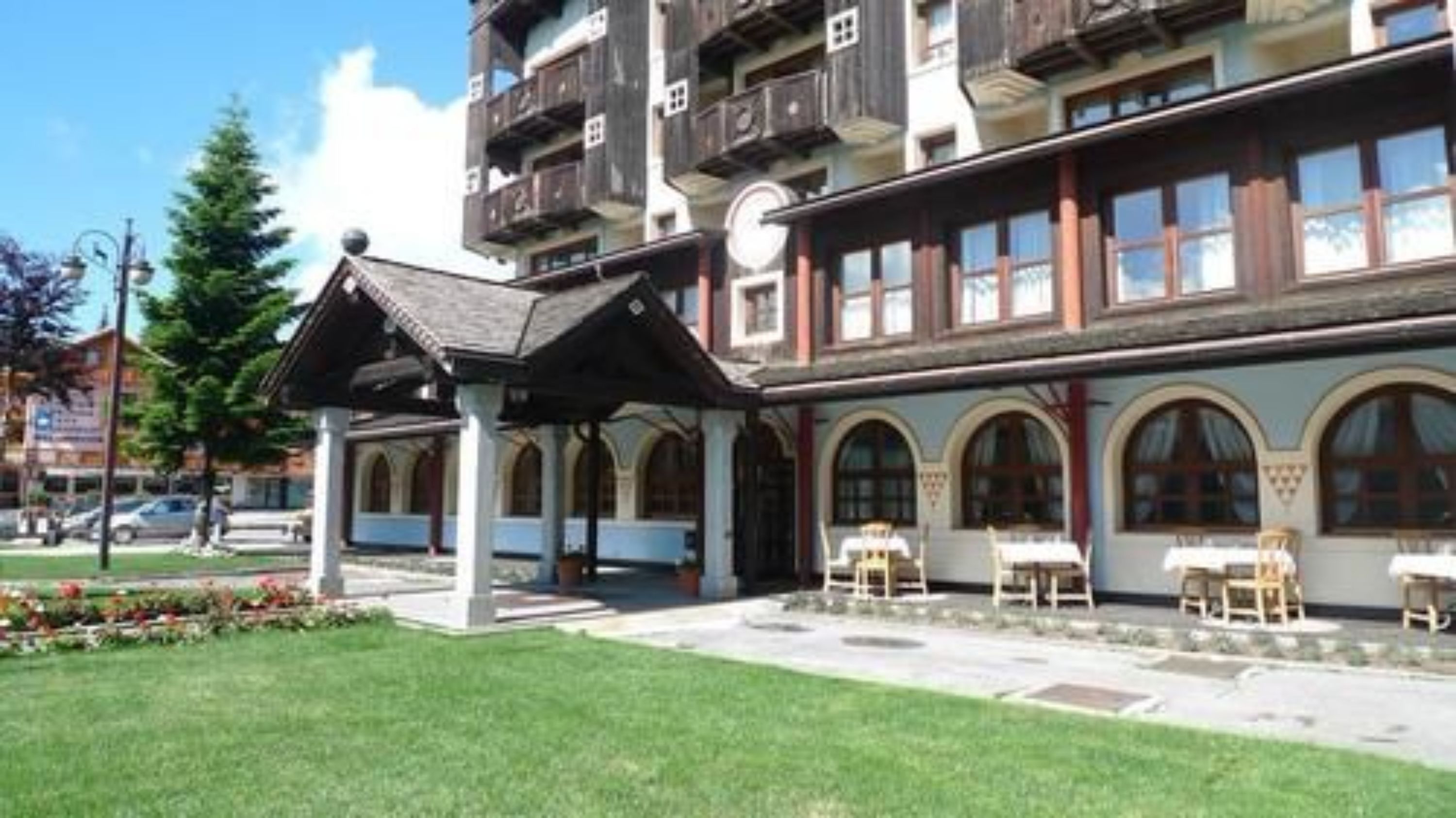 Un hotel con una zona de estar al aire libre techada, un jardín y un edificio con varios balcones y ventanas de arco.