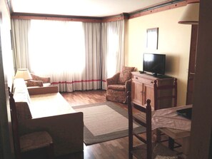A living room with a sofa, armchair, and a television on a wooden cabinet. - Hotel & Residence Catturani (Pinzolo)