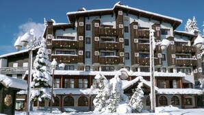 A multi-story hotel with a traditional Alpine architectural style, featuring wooden balconies and snow-covered trees. - Hotel & Residence Catturani (Pinzolo)