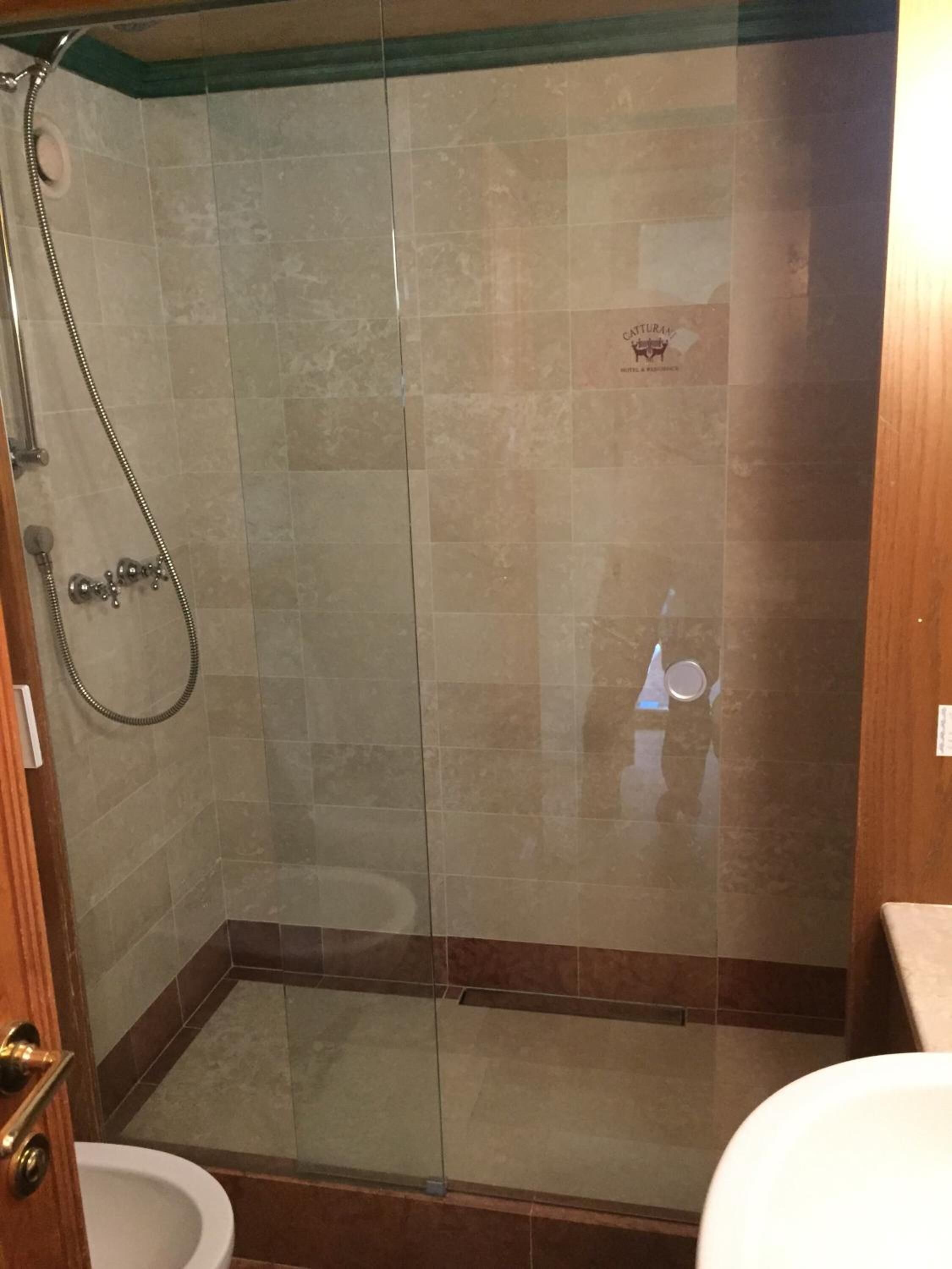 Een douche met glazen wanden, een betegelde vloer en een zichtbaar logo op de muur.