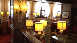 A warmly lit room with multiple lamps, a glass table, and red upholstered chairs. - Hotel & Residence Catturani (Pinzolo)