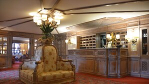 A grand lobby with a large ornate chair, a wooden reception desk, and a patterned carpet. - Hotel & Residence Catturani (Pinzolo)