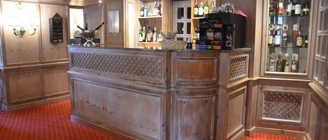 A bar area with a wooden counter, shelves with bottles, and a red patterned carpet.