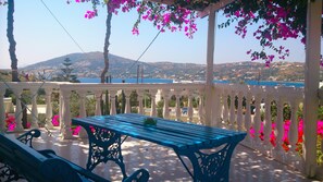 A balcony with a blue table and chairs, surrounded by white railings and pink flowers. - Angelika (Leros)