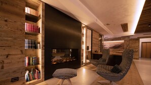 A modern living room with a wooden bookshelf, a fireplace, and patterned chairs. - Hotel Cristallo (Moena)