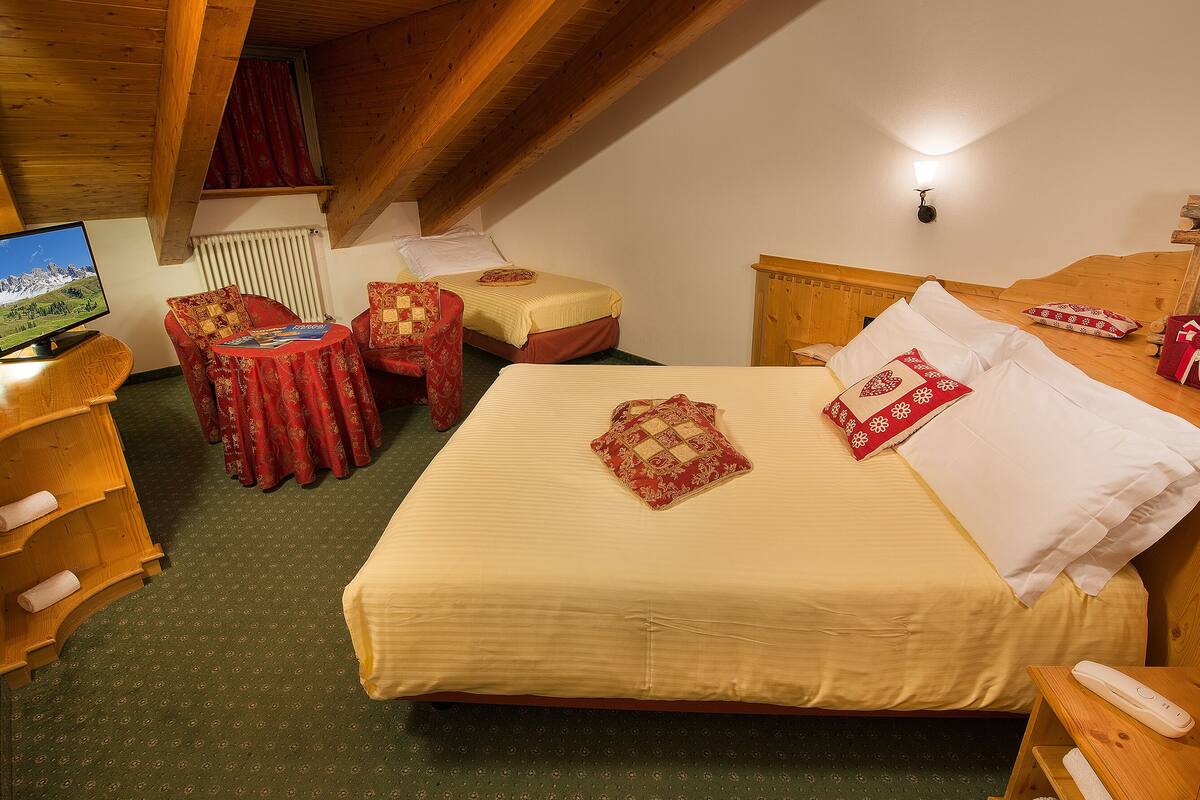 A cozy room with a bed, a chair, a small table, a TV, and a bedside table with a lamp.