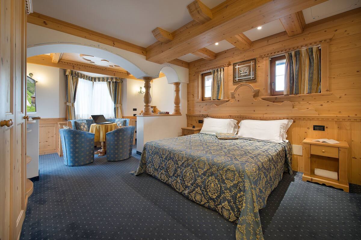 A wooden-paneled bedroom with a large bed, two chairs, a small table, and a nightstand.