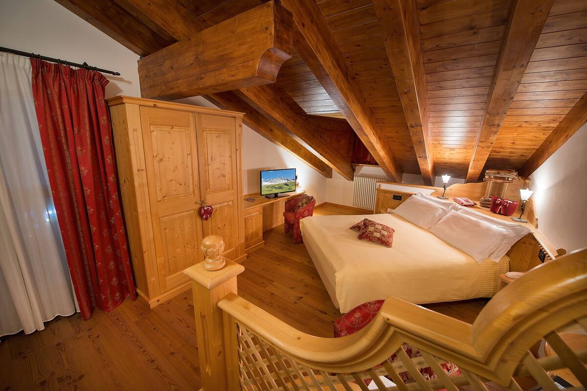A bedroom with a wooden ceiling, a bed, a wardrobe, and a television.
