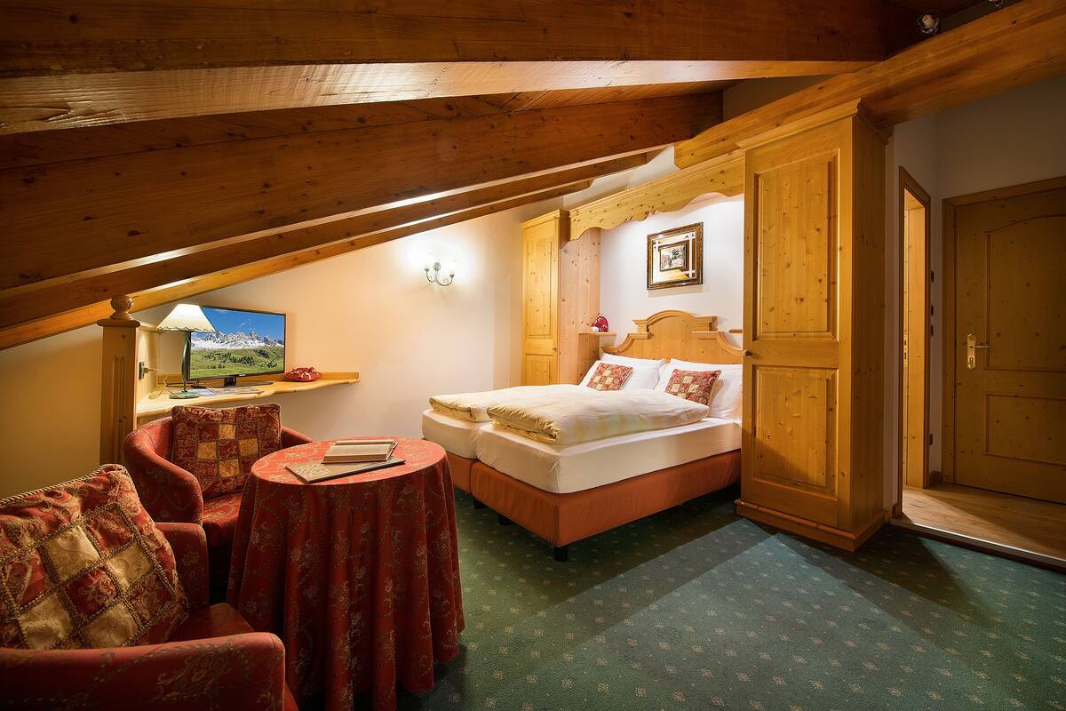 A bedroom with a bed, a chair, a table, and a wooden wardrobe.