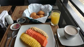 Uma mesa de café da manhã com um prato de frutas fatiadas, um copo de suco de laranja e uma xícara de café.