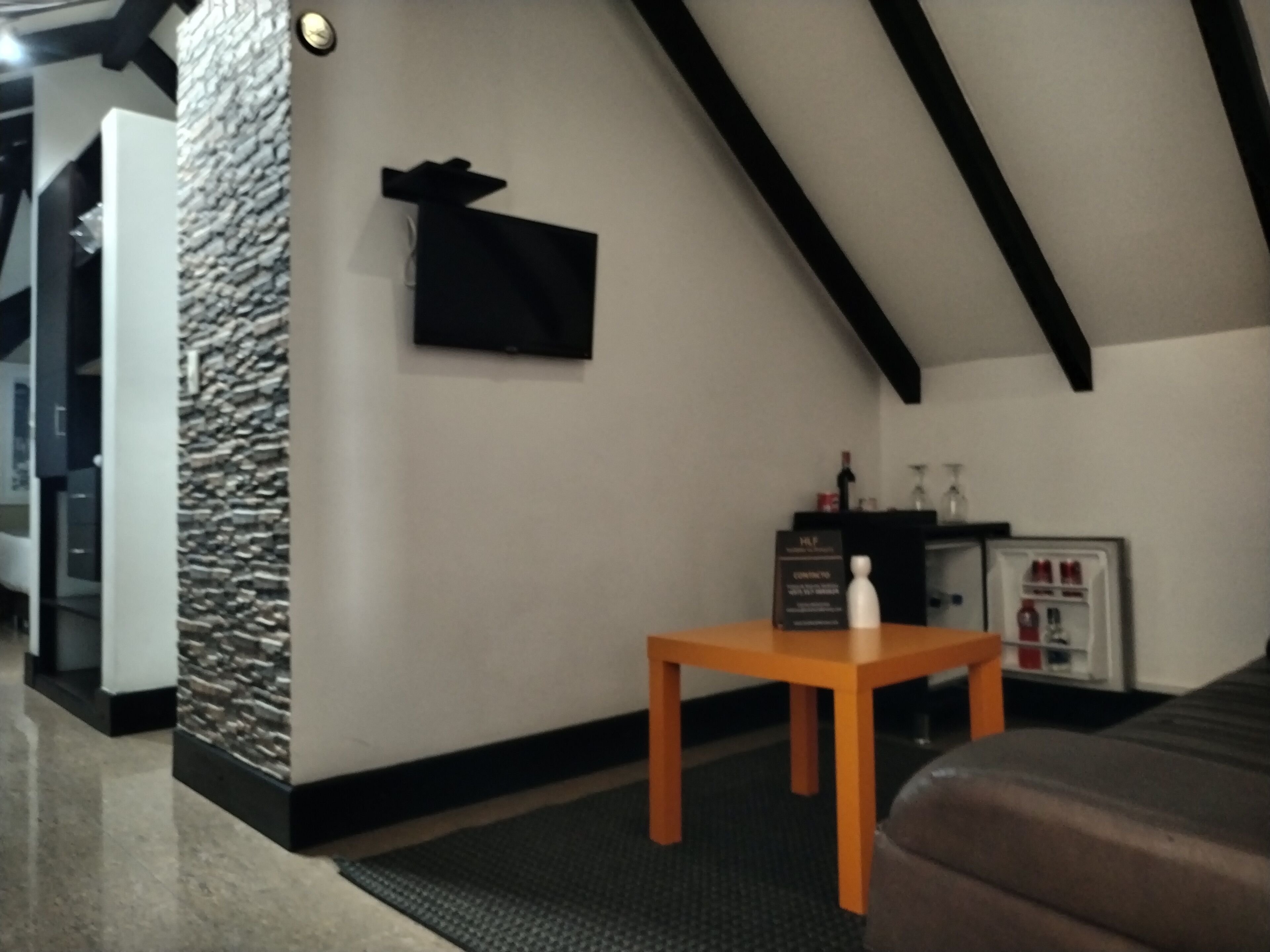 Een kamer met een accentmuur van steen, een zwart jasje hangend, een houten tafel en een bank.