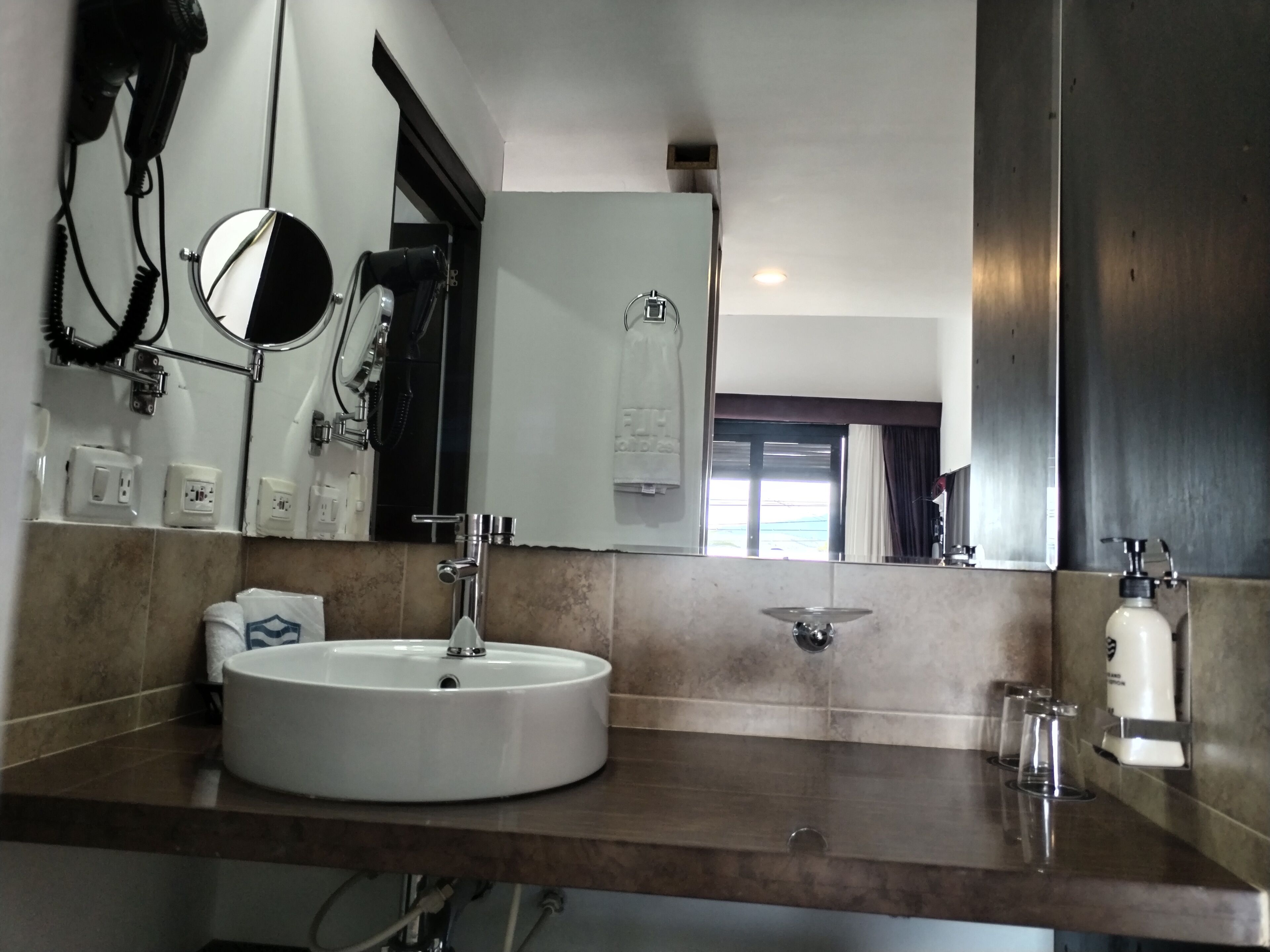 Uma casa de banho moderna com lavatório redondo, um espelho grande e um porta-toalhas.