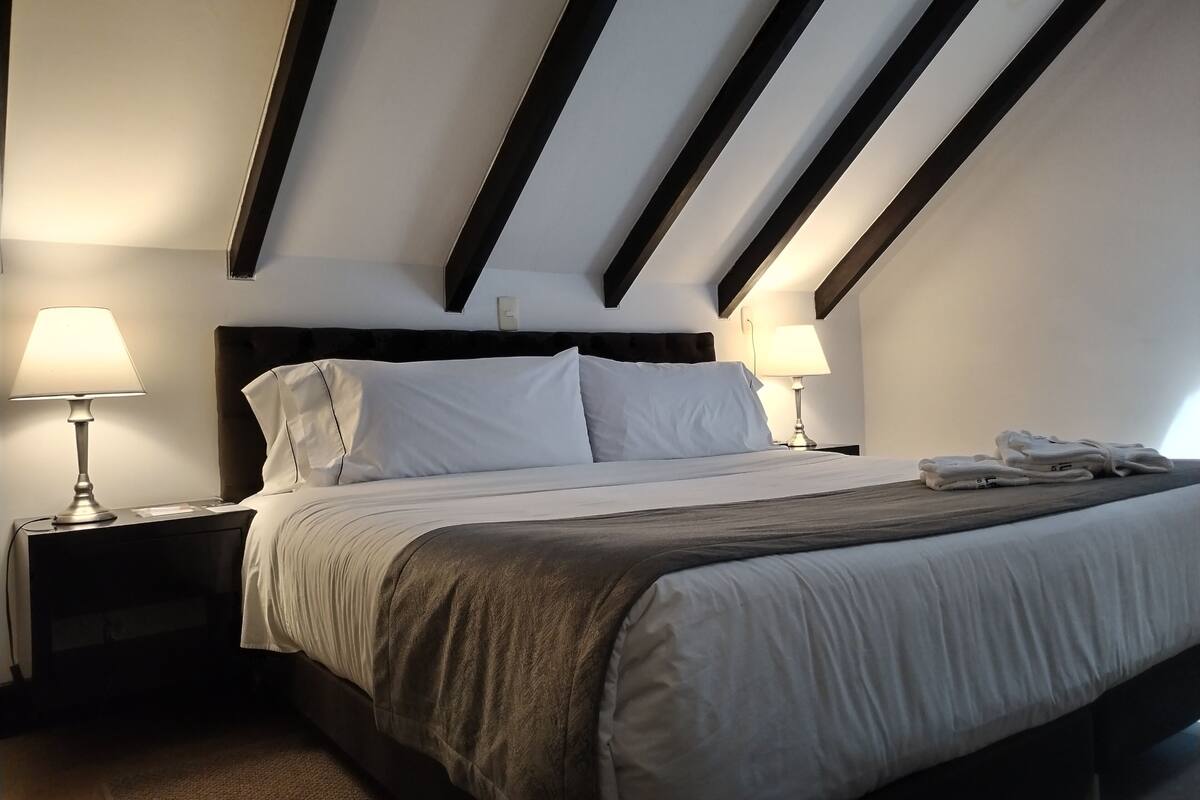 A hotel room with a bed, two bedside lamps, a headboard, and a neatly made bed.