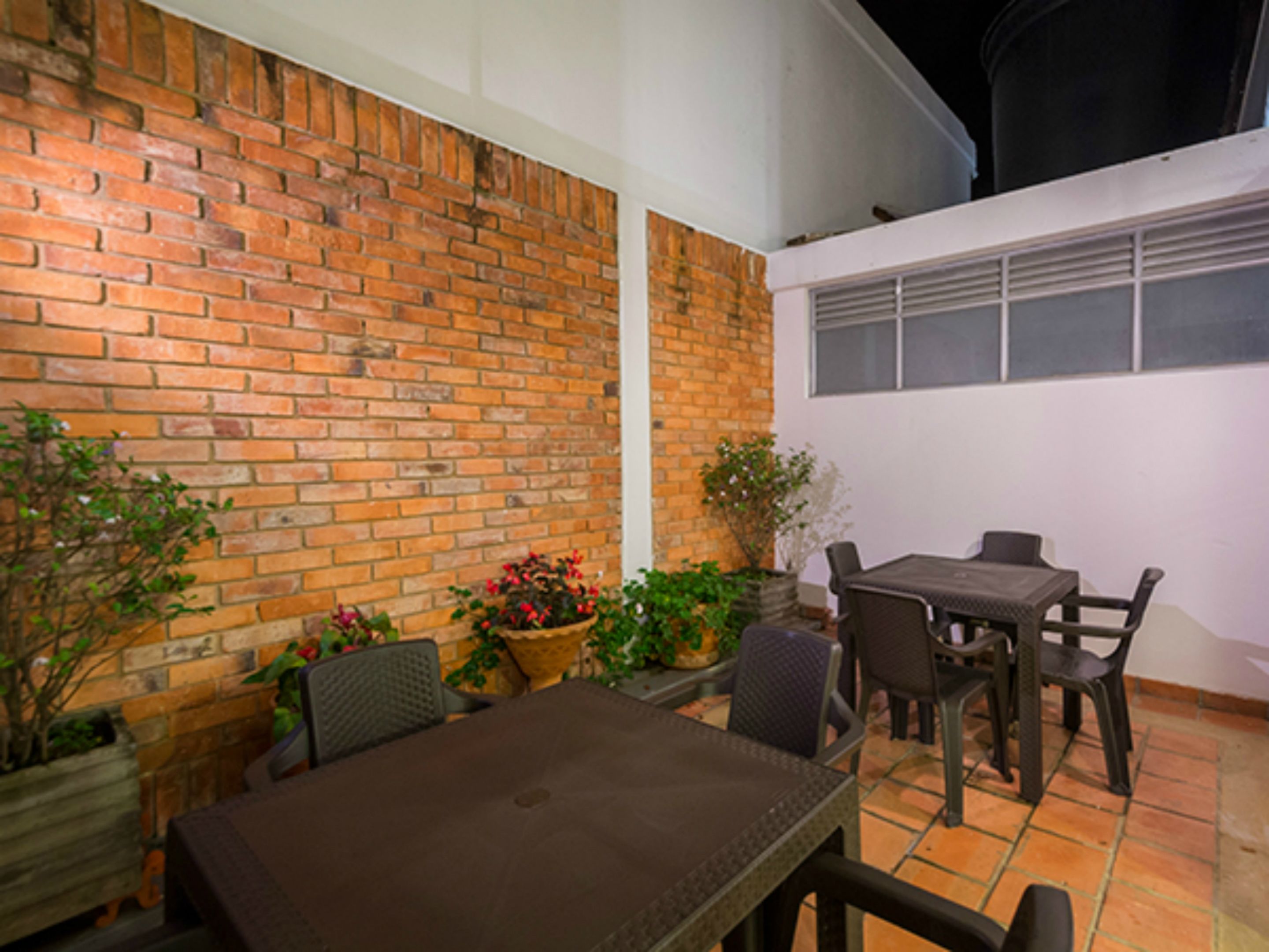 Une terrasse extérieure avec un mur en briques, une table et des chaises, ainsi que des plantes en pot.