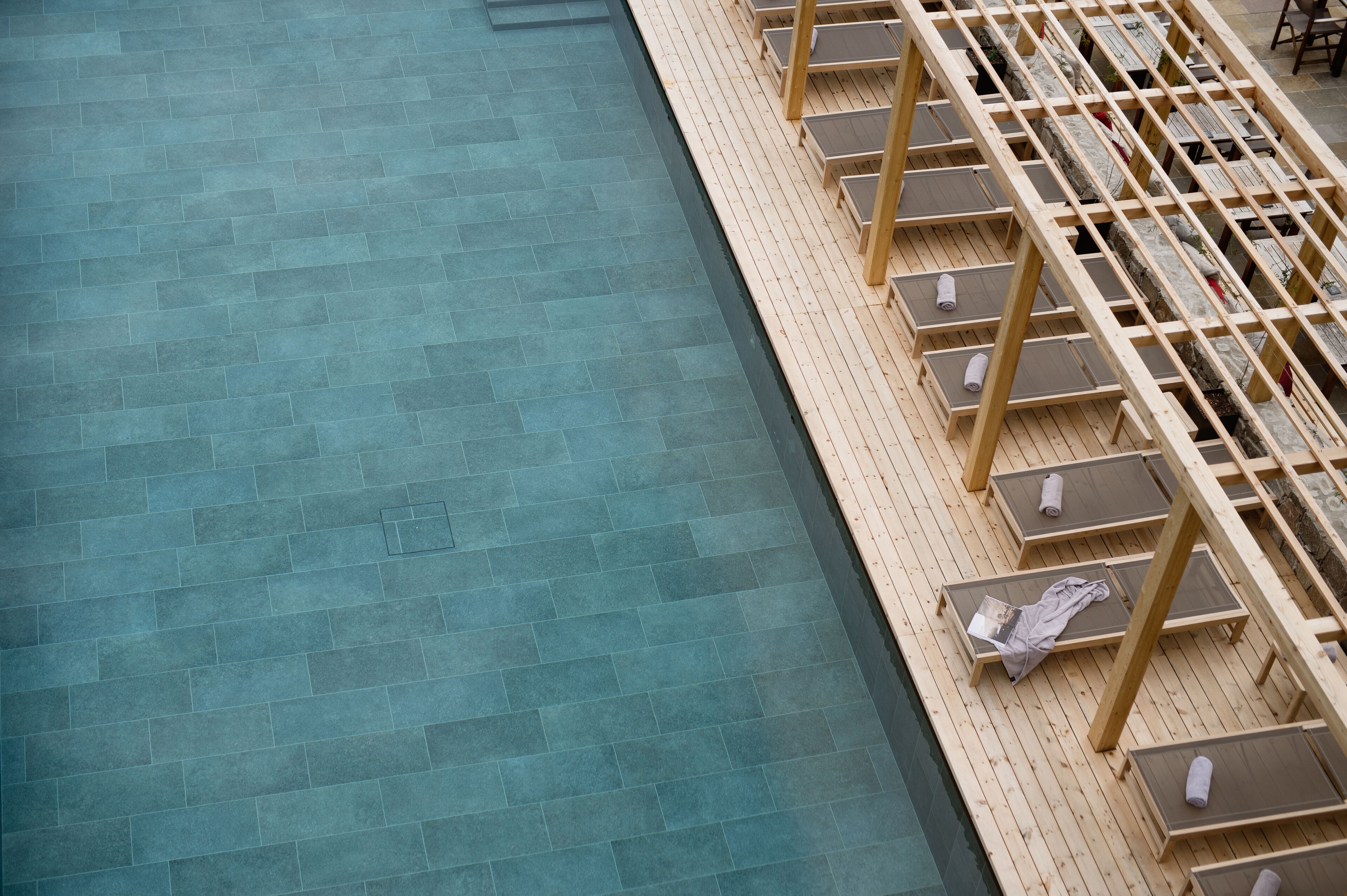 A poolside area with a tiled floor and wooden lounge chairs arranged in rows.