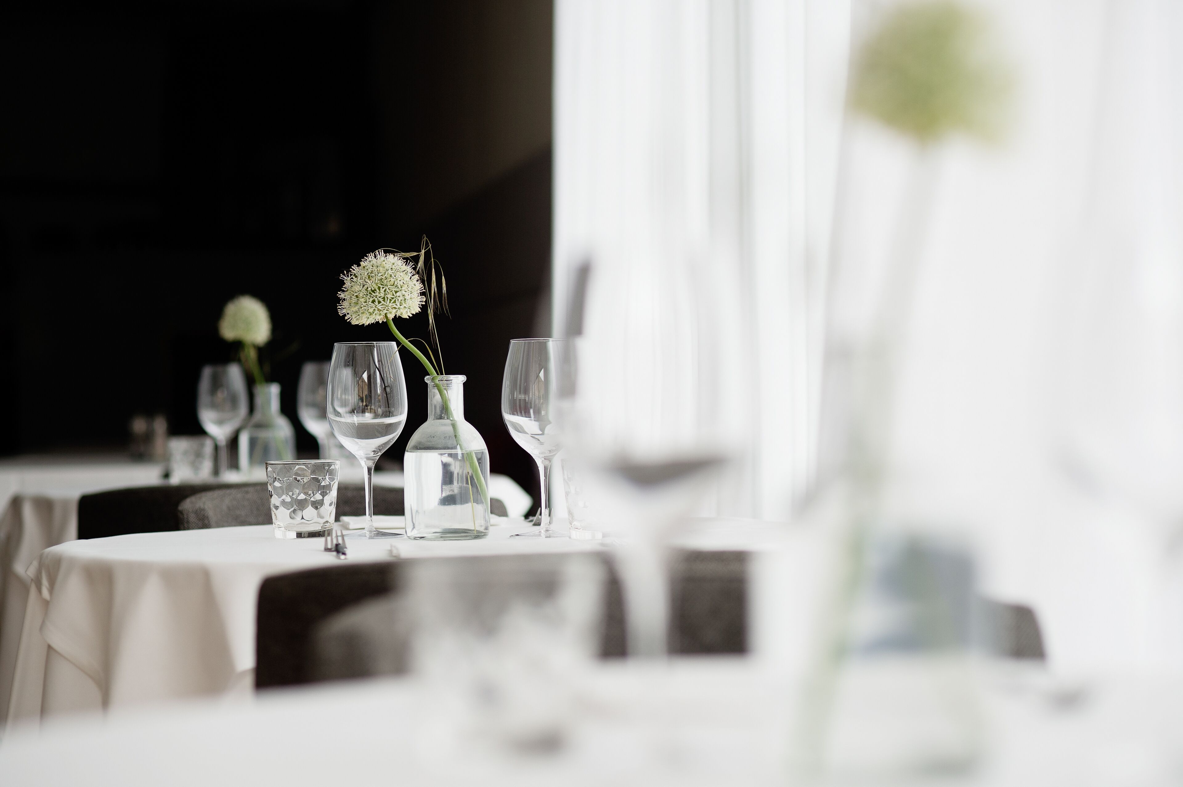 A table set with clear glassware and a single white flower, suggesting a formal dining setting.