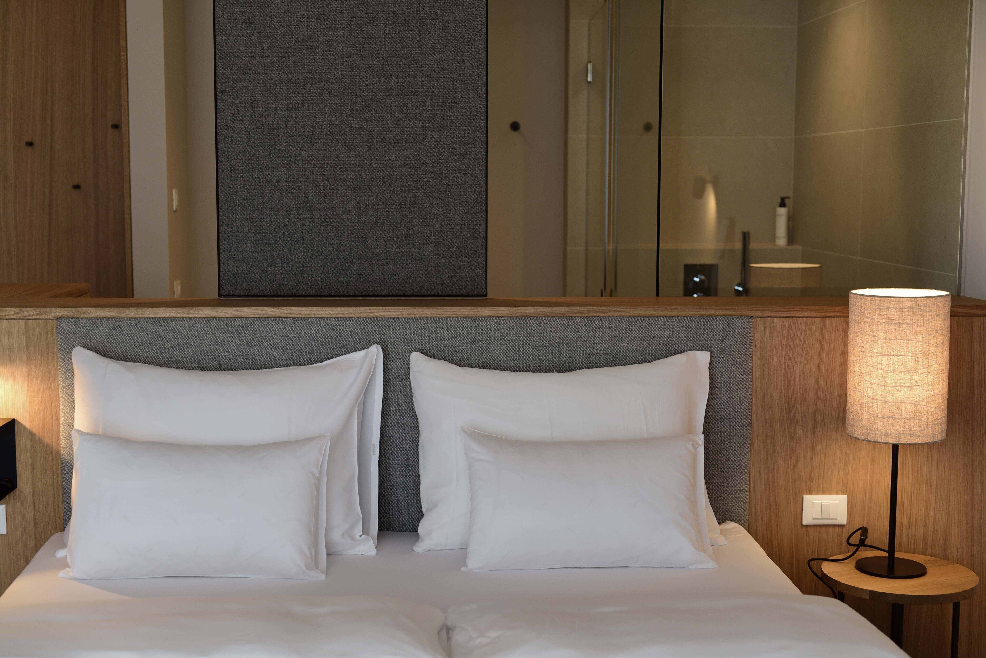 Et hotelværelse med en stor seng, to puder, et sengebord med en lampe og et spejl over sengen.