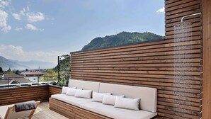 A wooden deck with a sofa and a cart, overlooking a mountainous landscape. - Hotel Schwarzschmied (Lana)