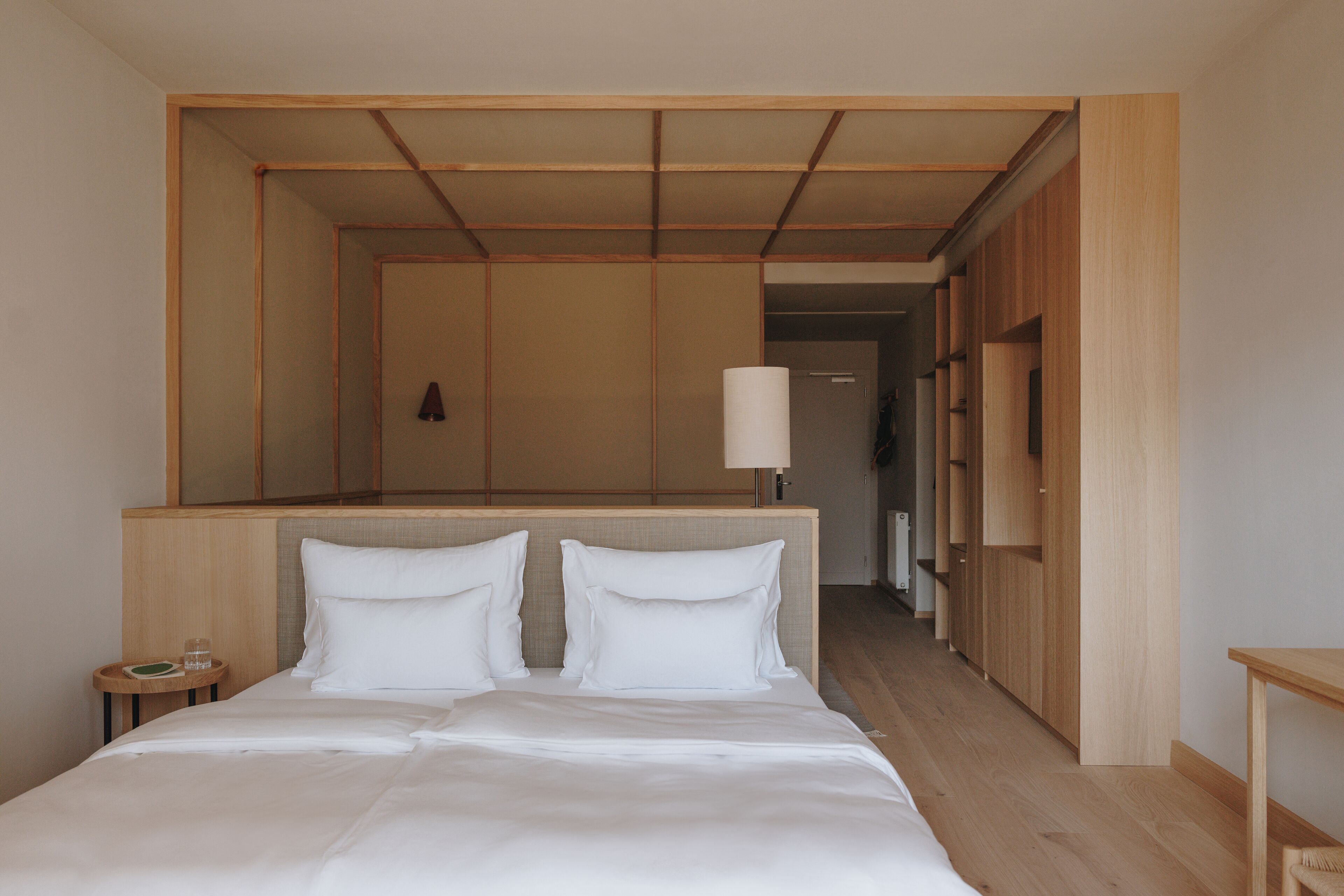 A hotel room with a large bed, a bedside table, a mirror, and a wooden wardrobe.