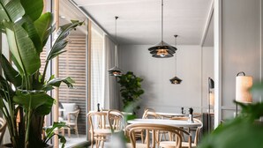 A modern dining area with wooden chairs and tables, pendant lighting, and large windows allowing natural light. - Hotel Schwarzschmied (Lana)