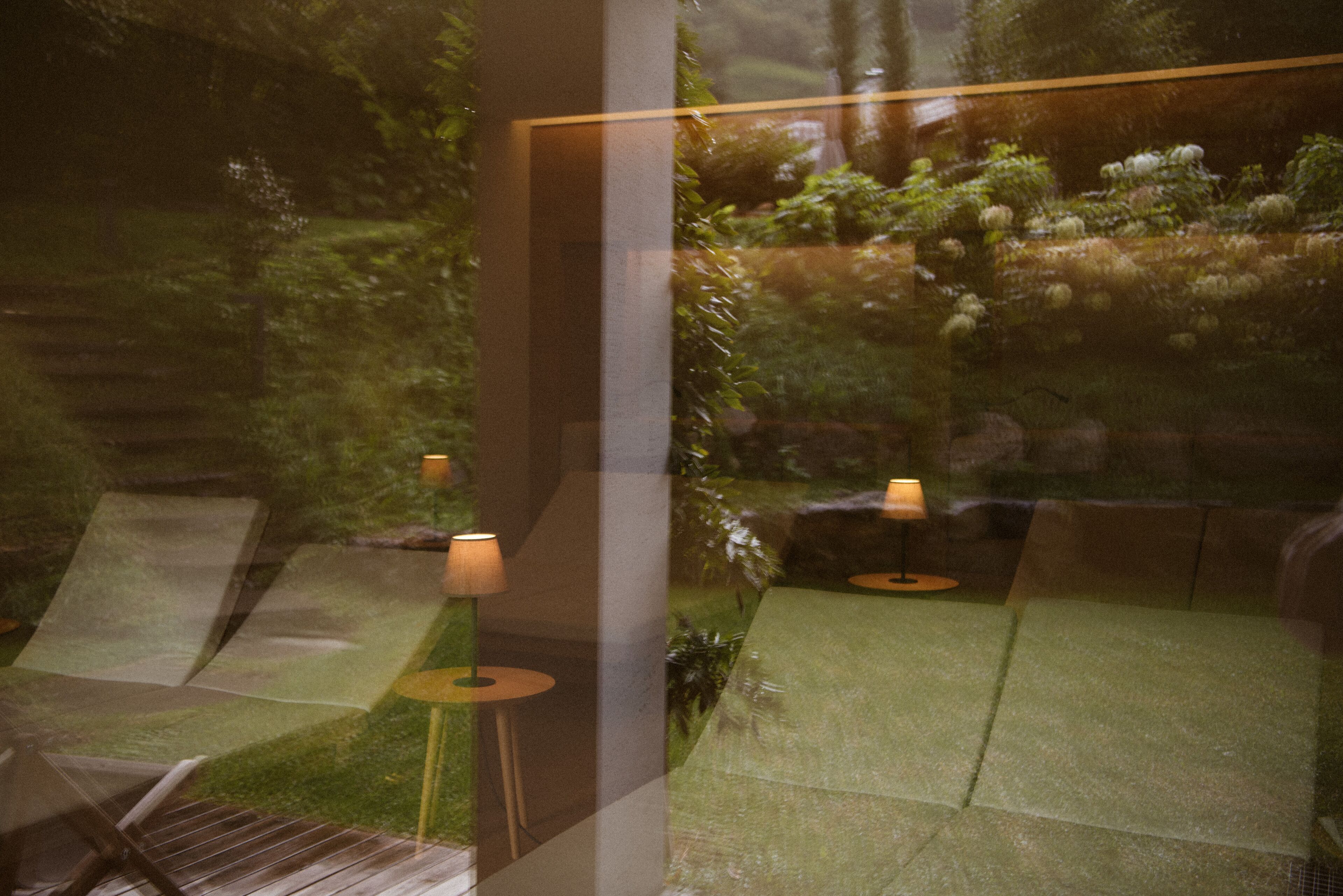 A view of a garden with a bench and a table, visible through a glass window.