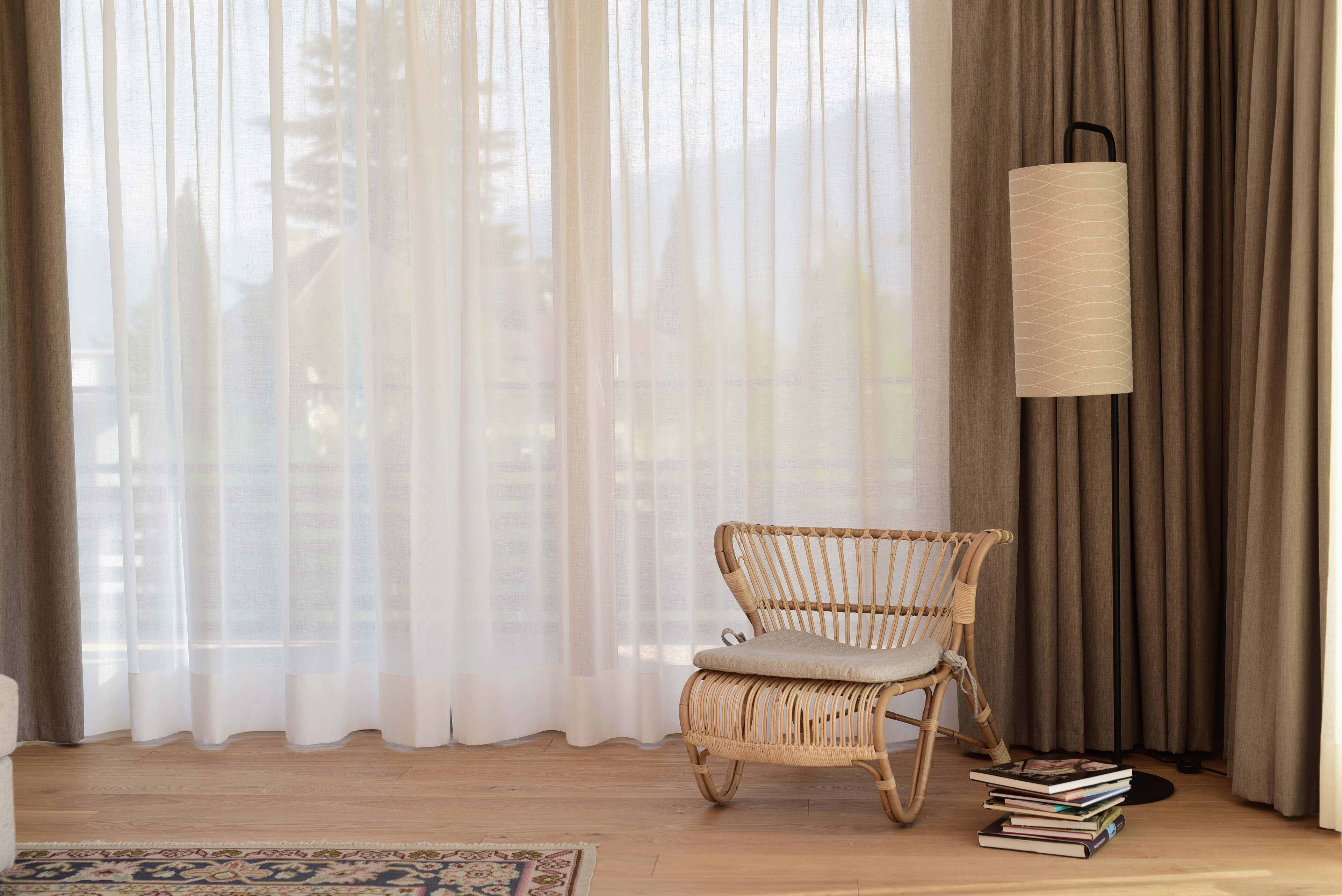 A room with a wicker chair, a floor lamp, and a stack of books.