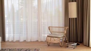 A room with a wicker chair, a floor lamp, and a stack of books.