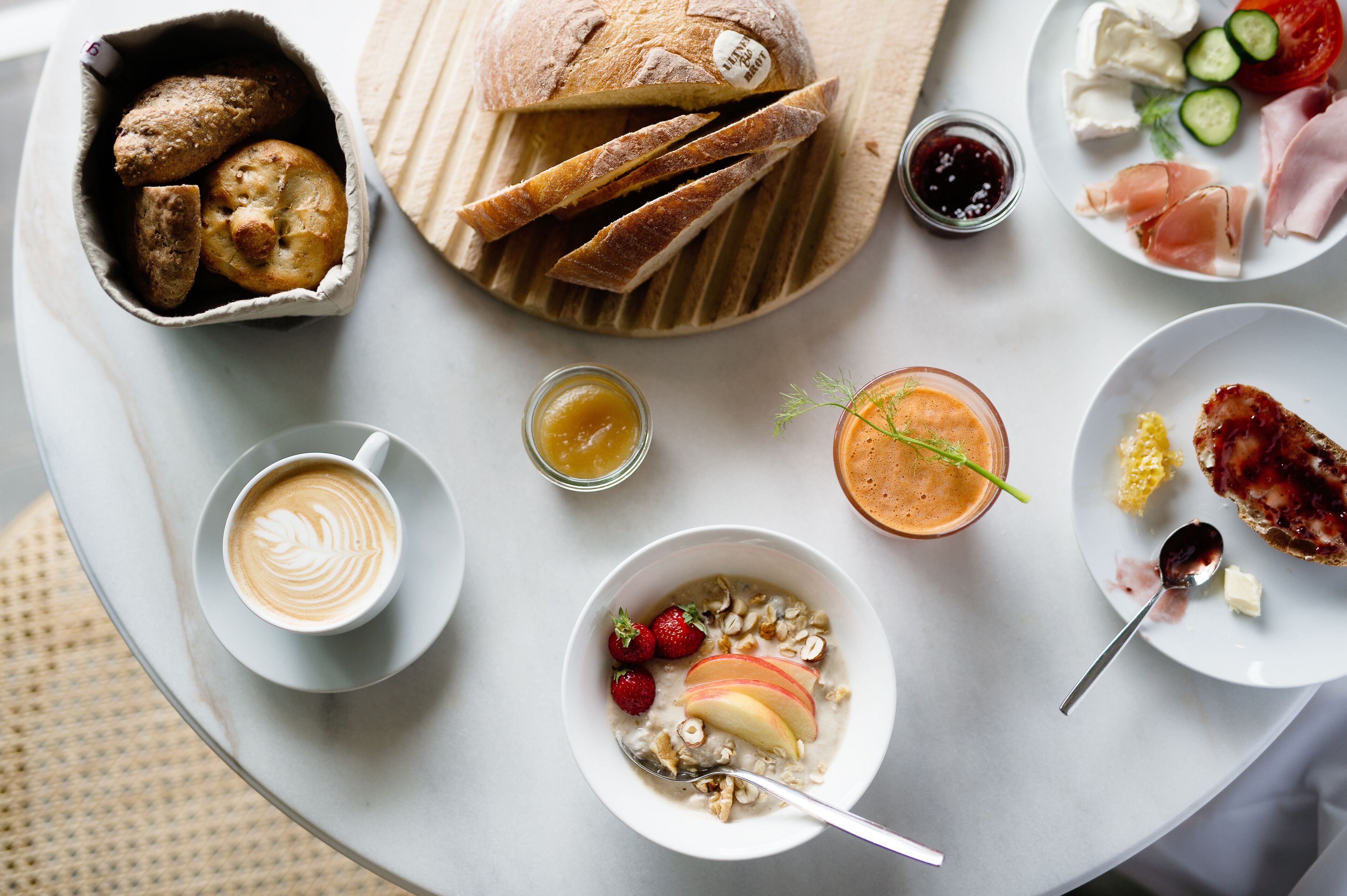 Una colazione con pane, pasticcini, formaggio, prosciutto e diversi tipi di frutta e bevande.
