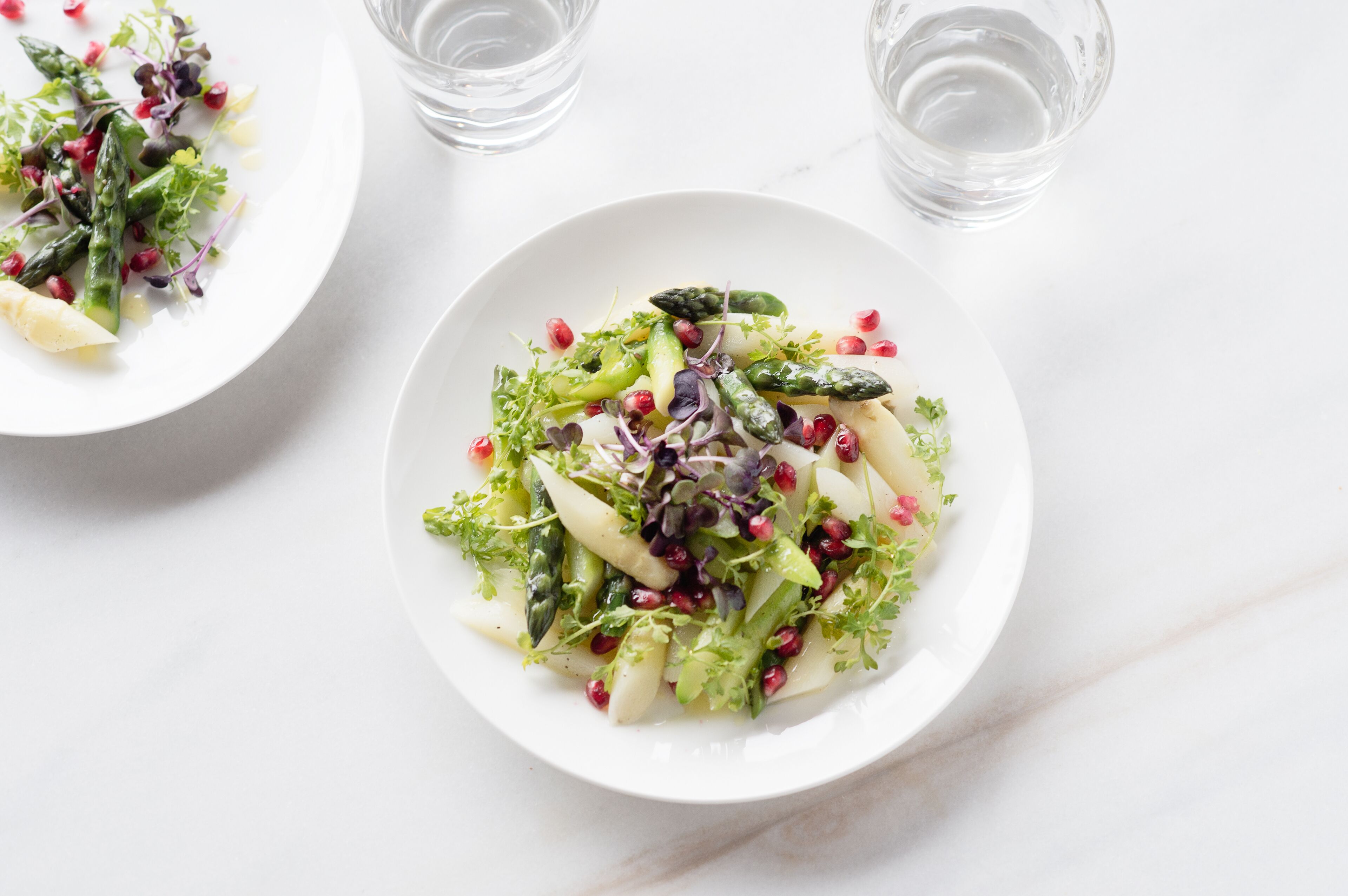 Two white plates with a salad on a white marble surface.