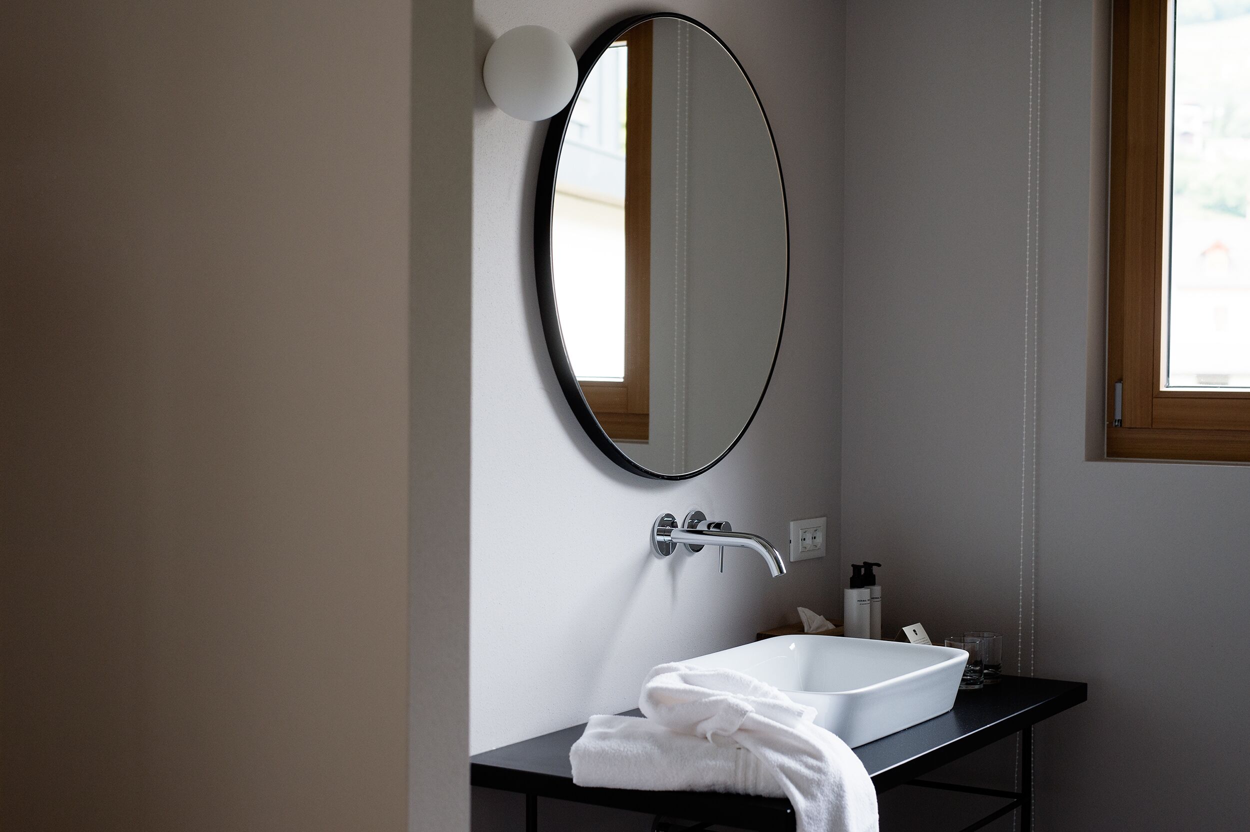 Un baño moderno con un lavamanos blanco, un espejo redondo y una toalla sobre el mostrador.