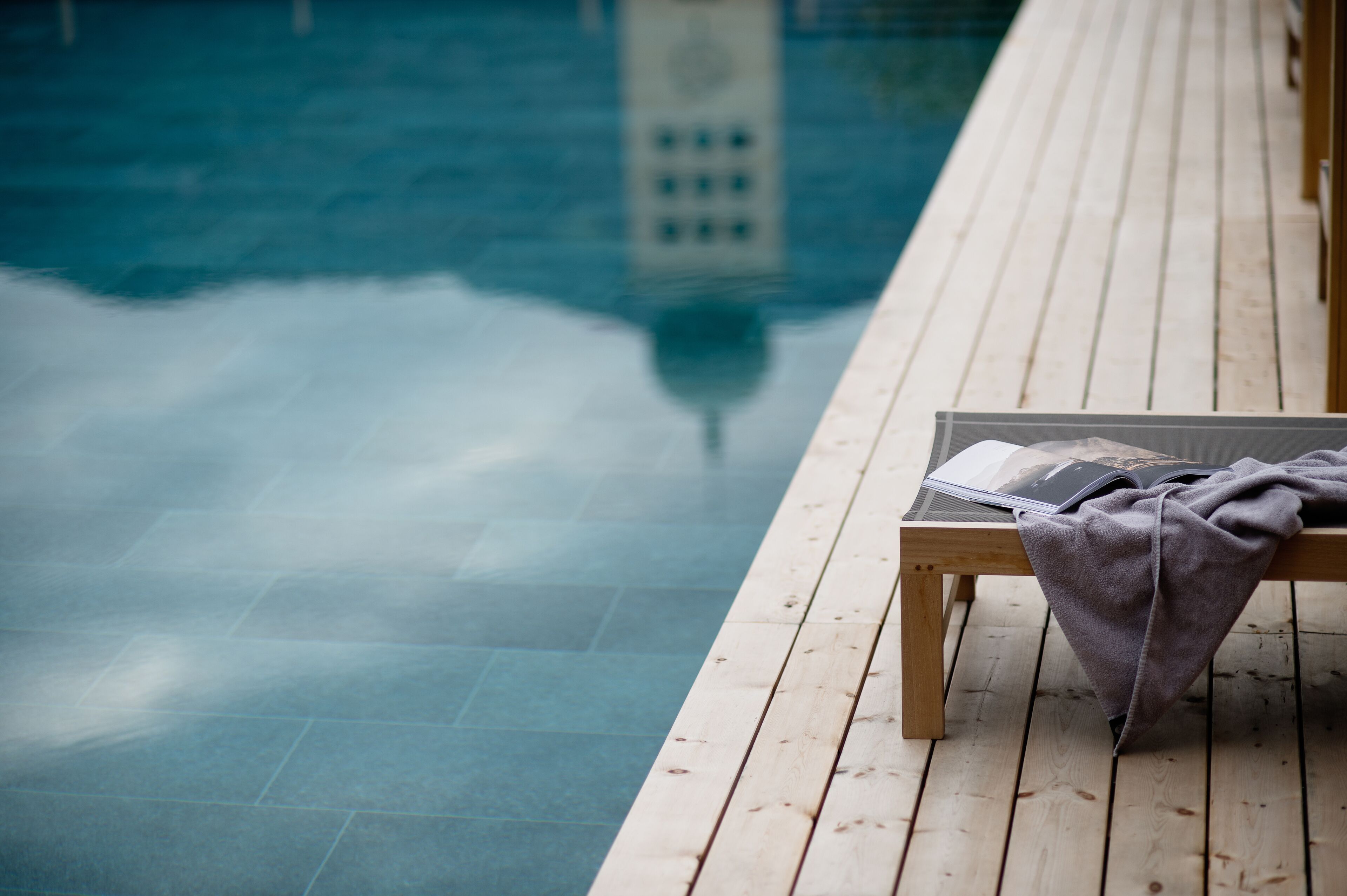 Eine Holzterrasse mit Pool und einer Liege, auf der eine Decke liegt.