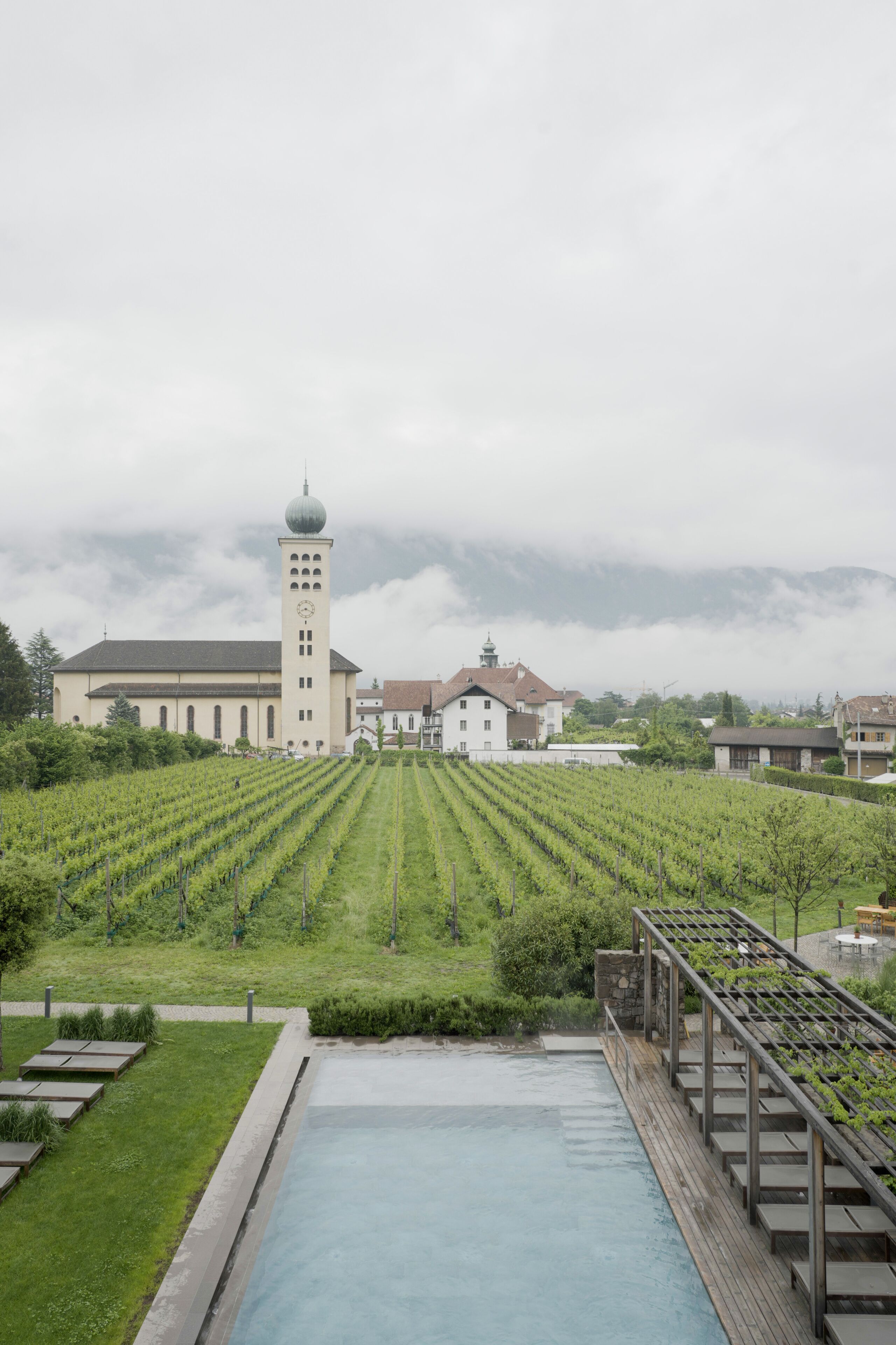 A large building with a tower, surrounded by well-maintained vineyards and a swimming pool.